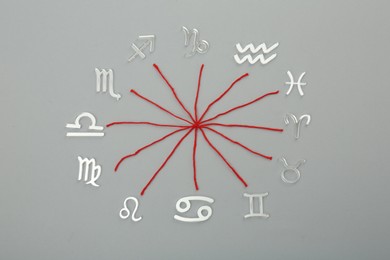 Zodiac compatibility. Signs and red threads on grey background, flat lay