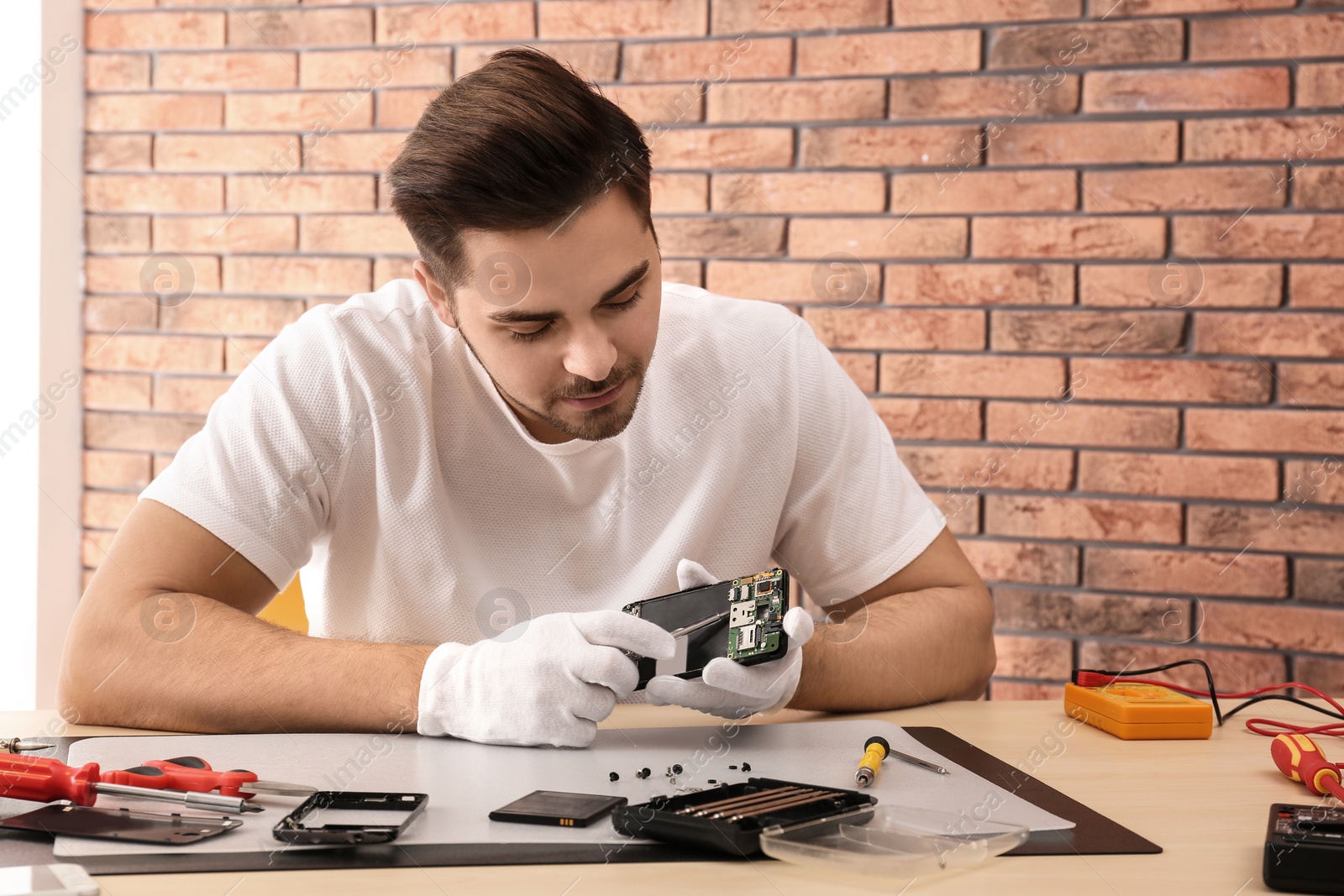 Photo of Technician repairing broken smartphone at table in workshop. Space for text