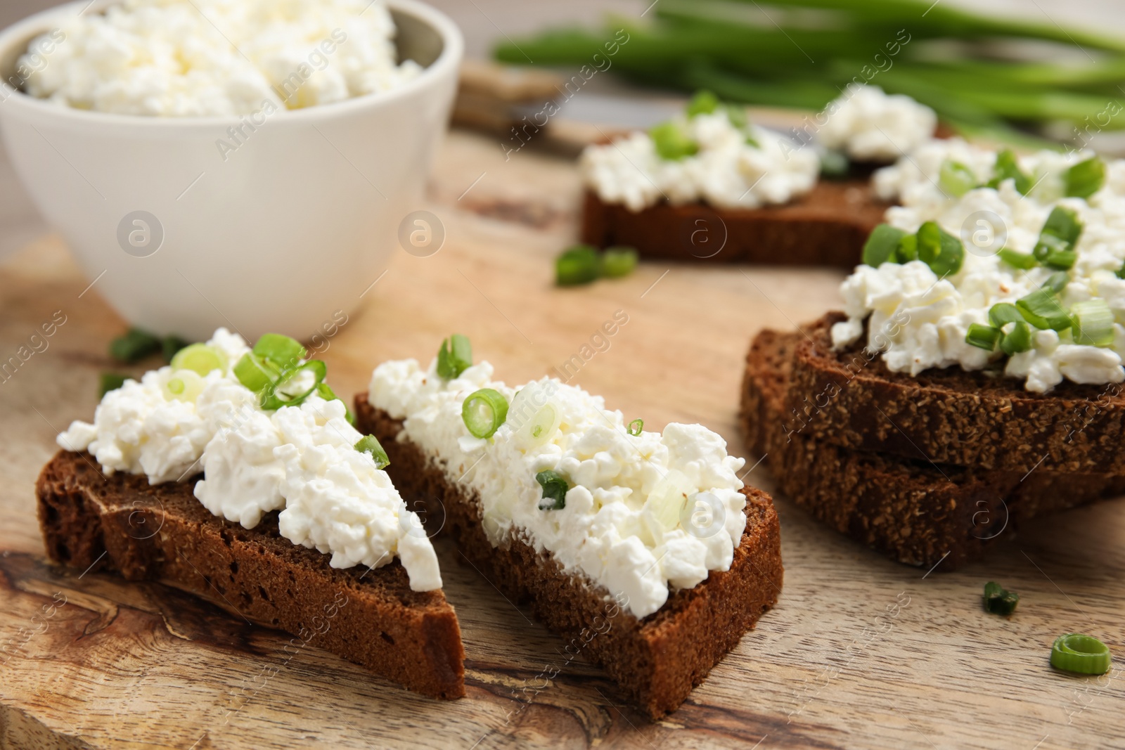 Photo of Bread with cottage cheese and green onion on wooden table, closeup