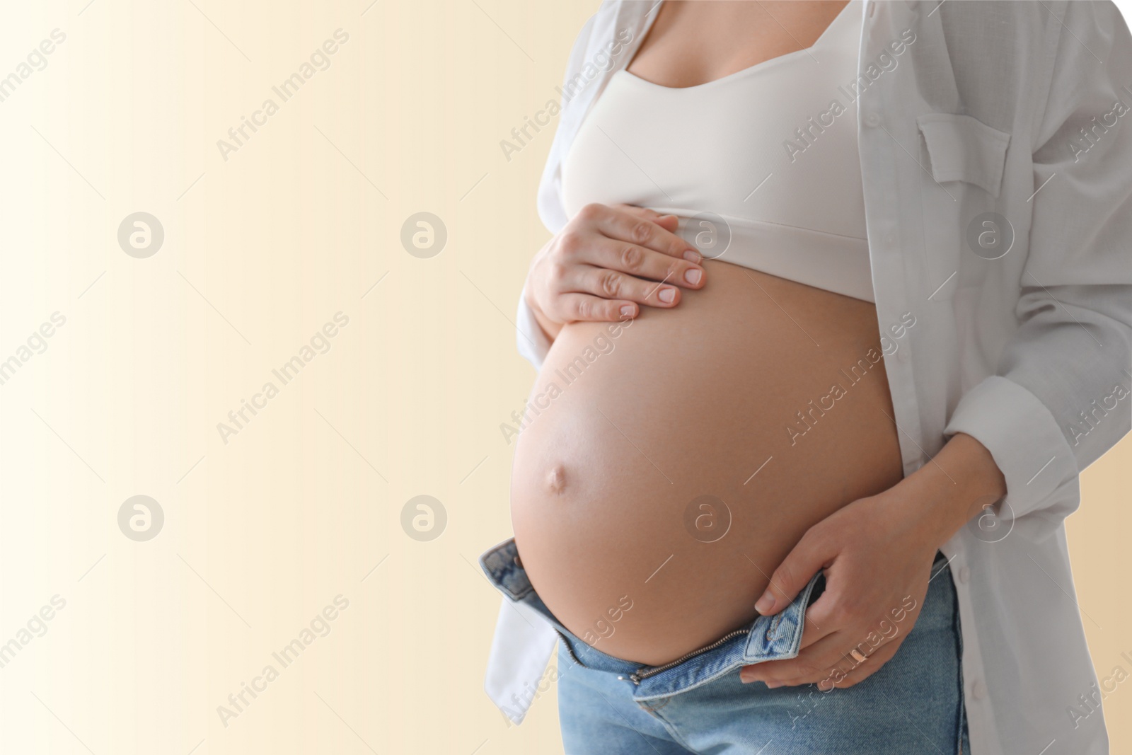 Image of Young pregnant woman touching her belly on beige background, closeup. Space for text