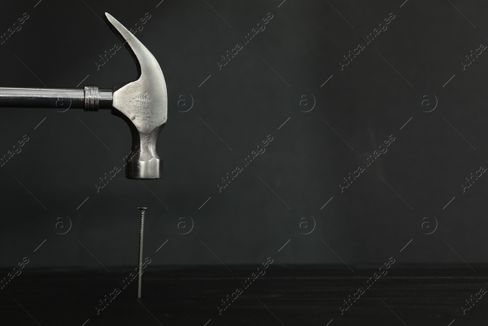 Photo of Hammering metal nail on wooden table against black background. Space for text