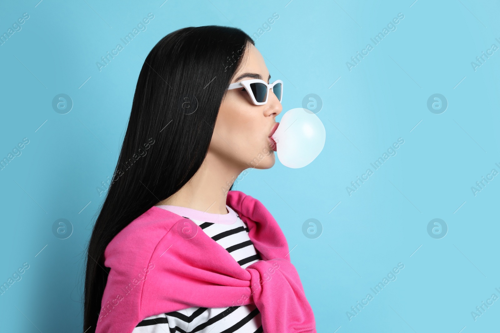 Photo of Fashionable young woman blowing bubblegum on light blue background, space for text