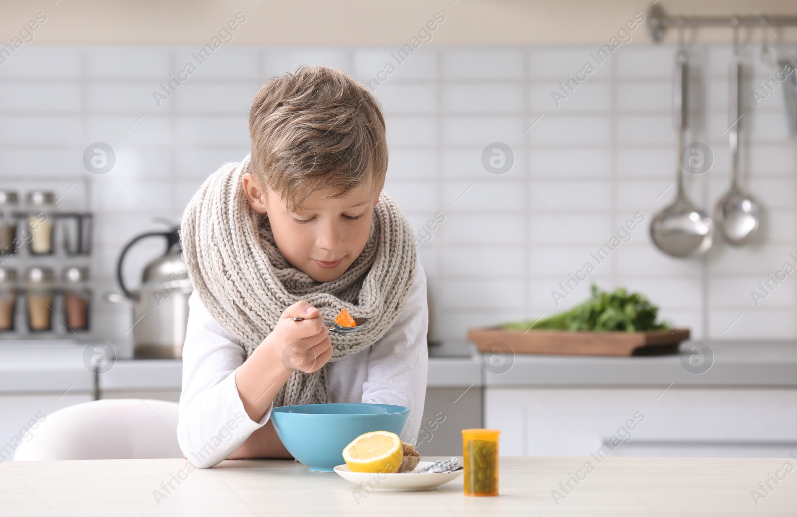 Photo of Sick little boy eating broth to cure cold at table in kitchen