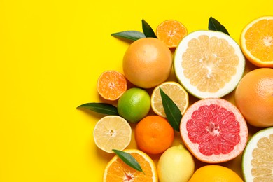 Photo of Different ripe citrus fruits with green leaves on yellow background, flat lay. Space for text