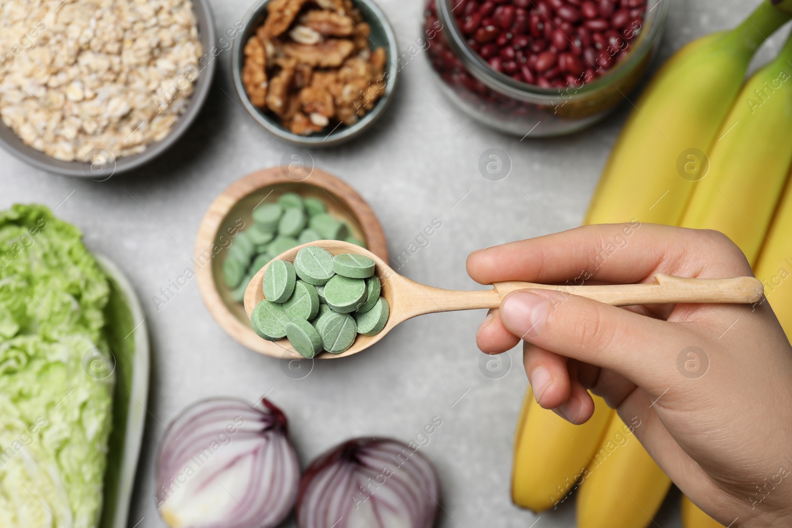 Photo of Woman holding spoon of pills at table with foodstuff, top view. Prebiotic supplements