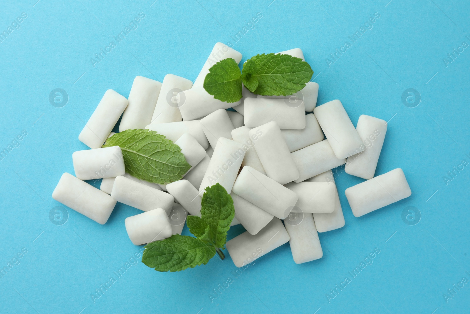 Photo of Pile of tasty white chewing gums and mint leaves on light blue background, top view