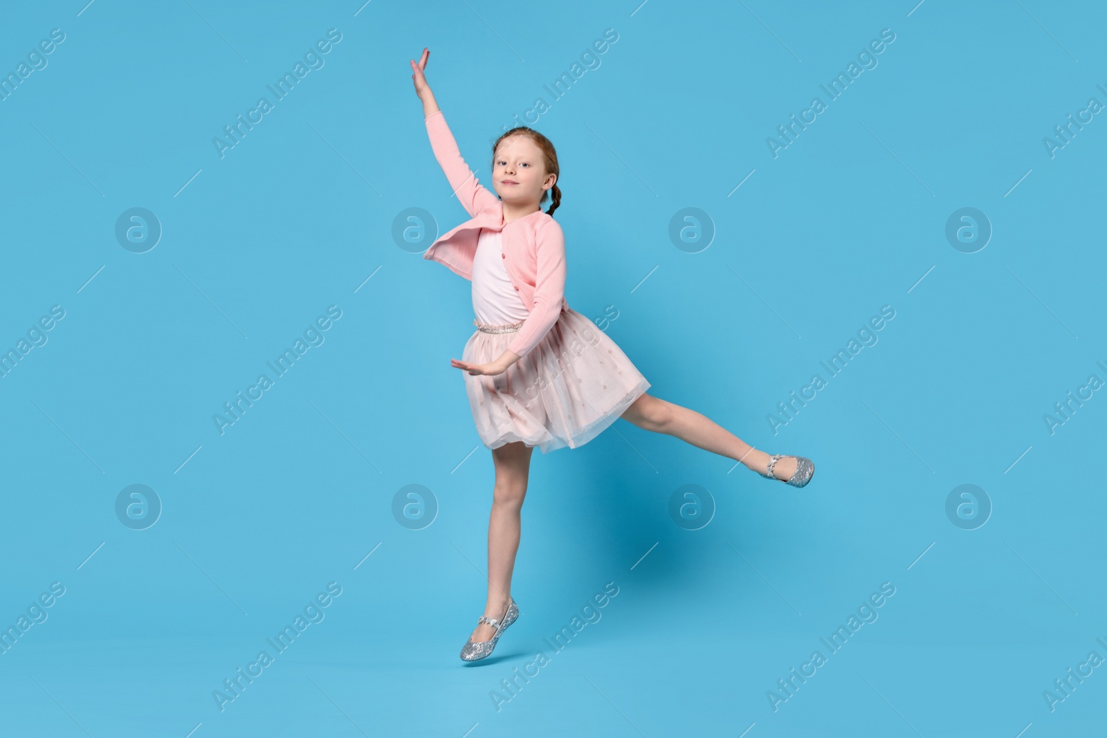 Photo of Cute little girl dancing on light blue background