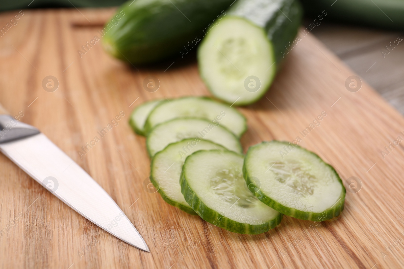 Photo of Cut cucumber and knife on wooden board, closeup