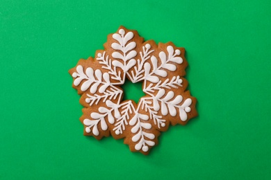Photo of Christmas snowflake shaped gingerbread cookie on green background, top view