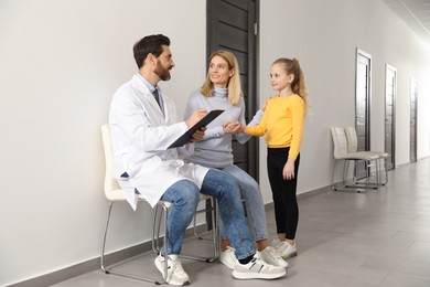 Photo of Doctor with clipboard consulting mother and daughter in clinic