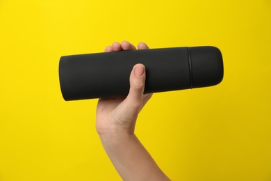 Photo of Woman holding modern black thermos on yellow background, closeup