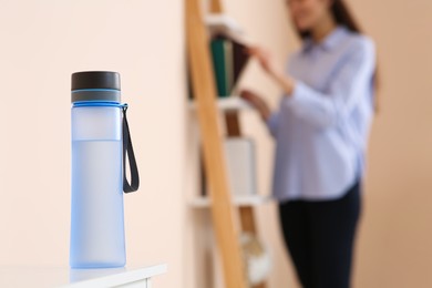 Young woman near shelving unit indoors, focus on bottle