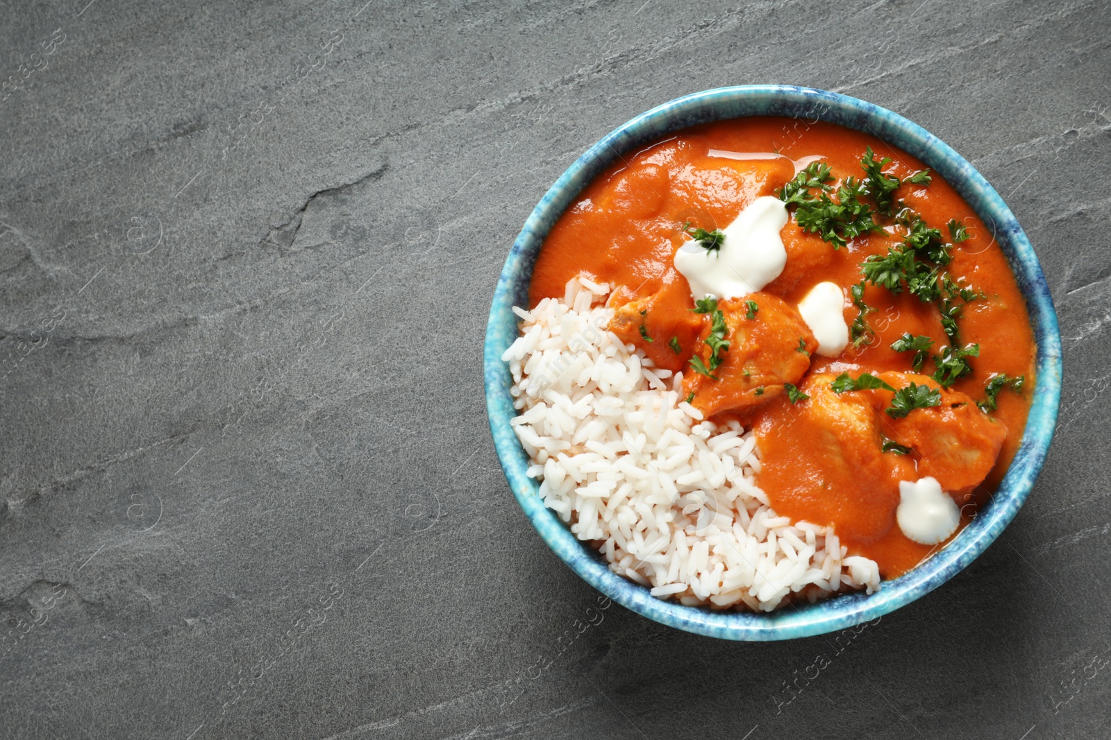 Photo of Delicious butter chicken with rice in bowl on grey background, top view. Space for text