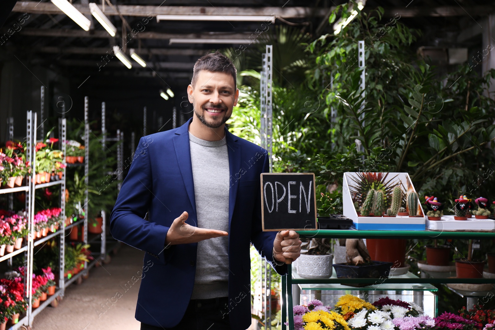 Photo of Male business owner holding OPEN sign in his flower shop