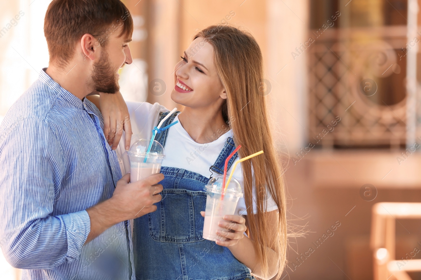 Photo of Young couple with cups of delicious milk shake outdoors