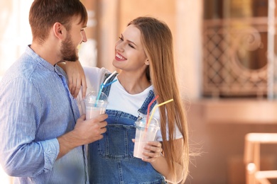 Young couple with cups of delicious milk shake outdoors