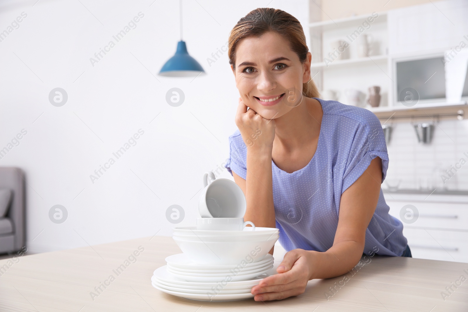 Photo of Woman with stack of clean dishes at kitchen table. Space for text