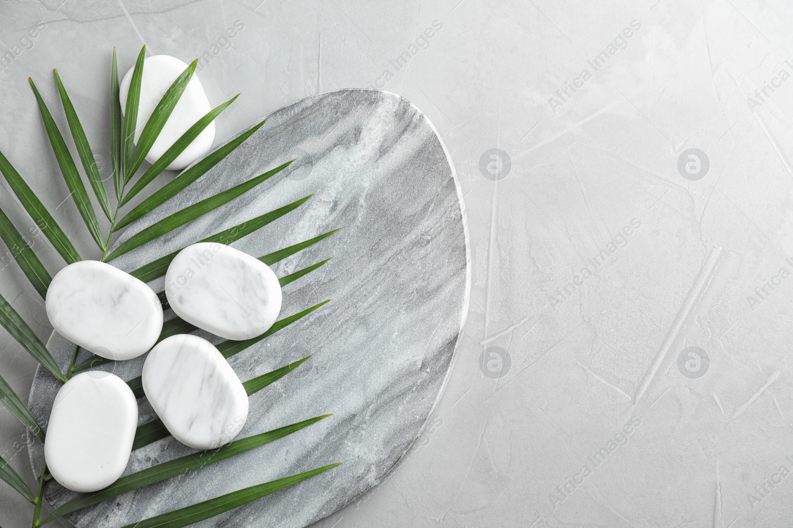 Photo of Flat lay composition with spa stones and palm leaf on grey table, space for text