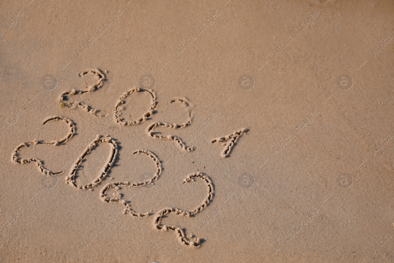 Photo of 2021 and 2022 written on sand at beach, above view. New Year celebration