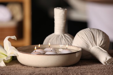 Photo of Spa composition with burning candles, lily flower and herbal bags on massage table in wellness center, closeup