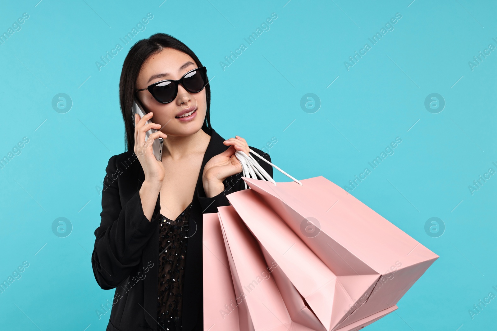 Photo of Smiling woman with shopping bags talking by smartphone on light blue background