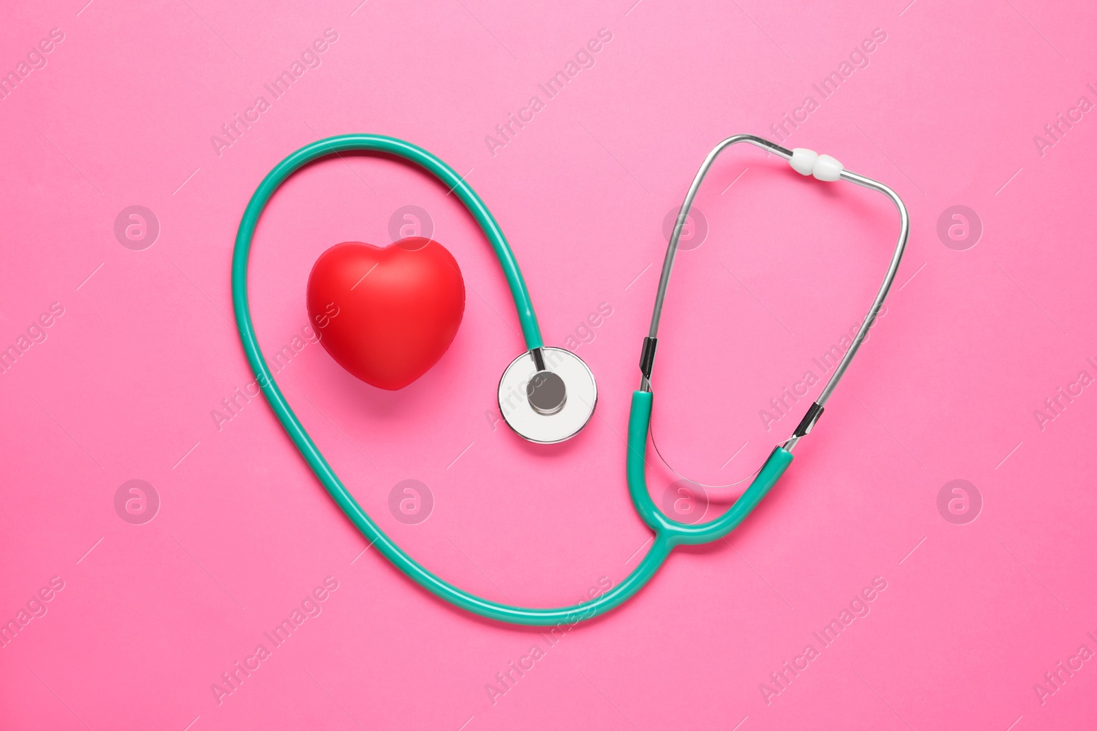 Photo of Stethoscope and red decorative heart on pink background, flat lay. Cardiology concept