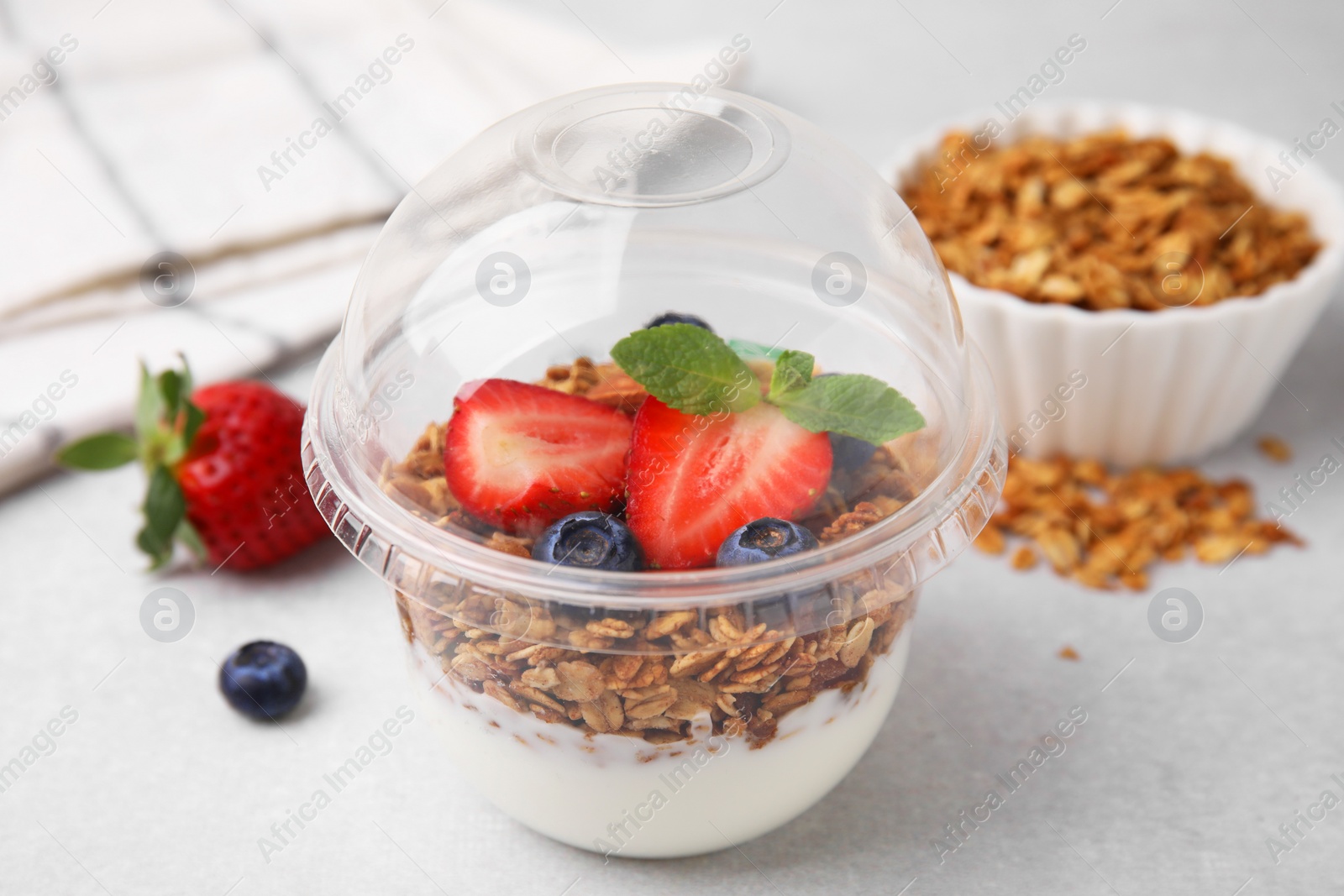 Photo of Tasty granola with berries and yogurt in plastic cup on light table, closeup