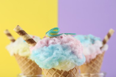 Photo of Sweet cotton candies in waffle cones and marshmallows on color background, closeup