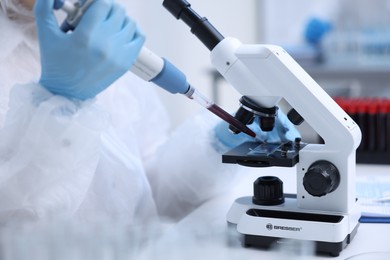 Scientist dripping sample onto glass slide while working with microscope in laboratory, closeup