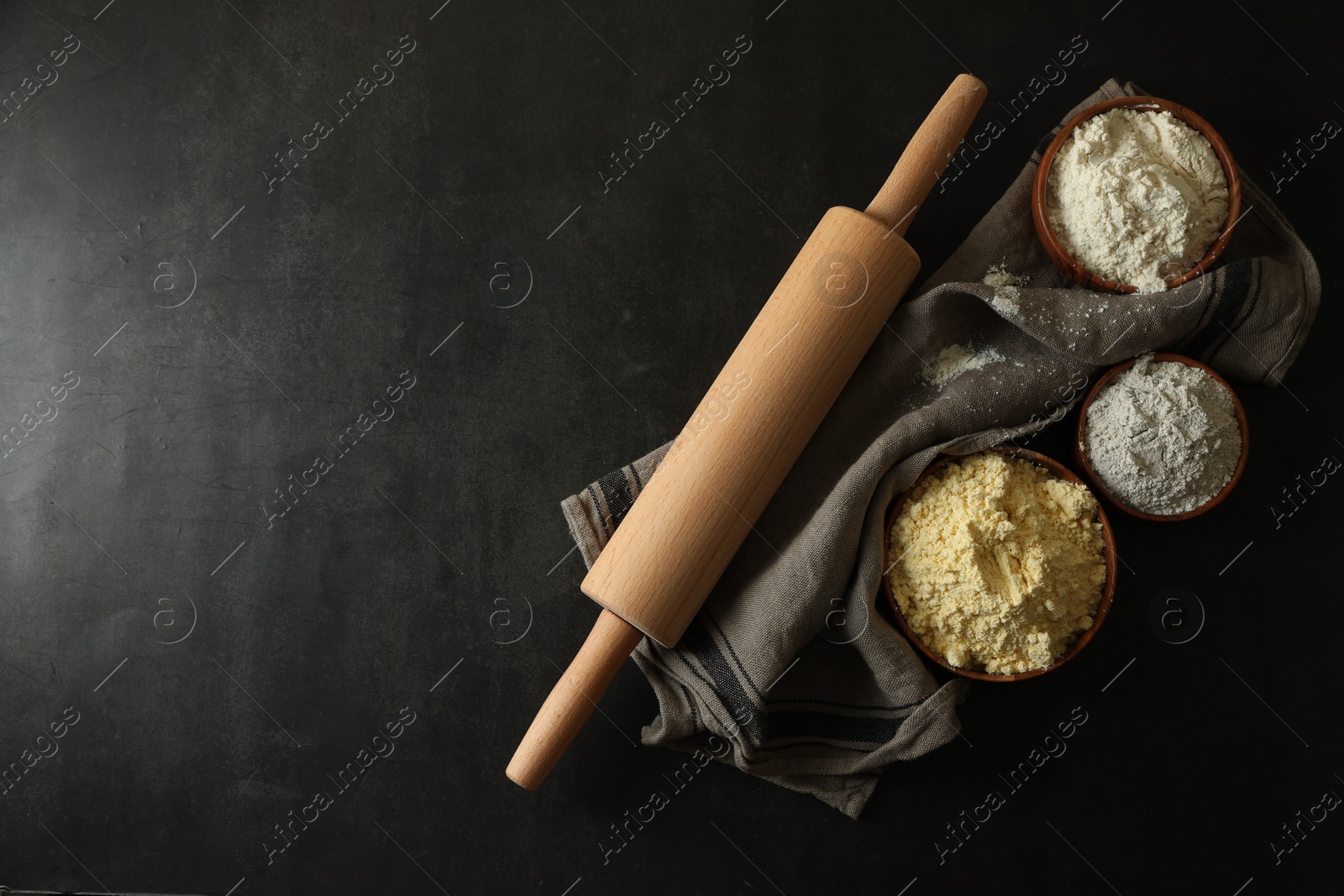 Photo of Rolling pin and different types of flour on black table, top view. Space for text