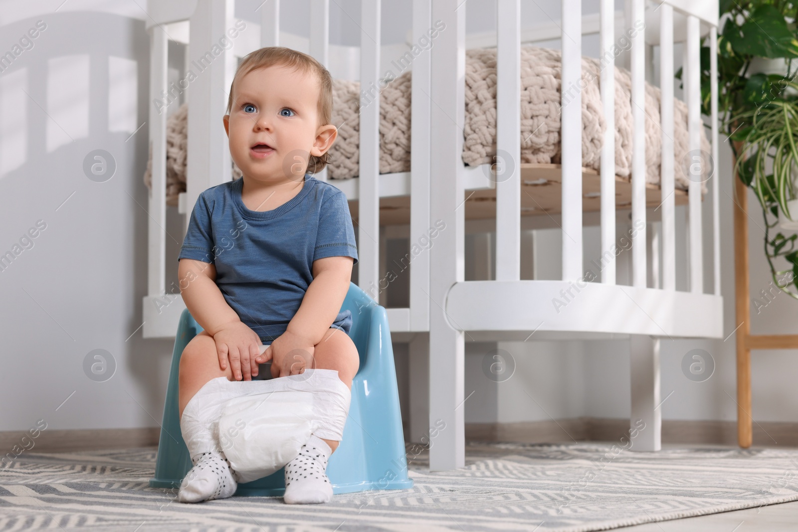 Photo of Little child sitting on plastic baby potty indoors. Space for text