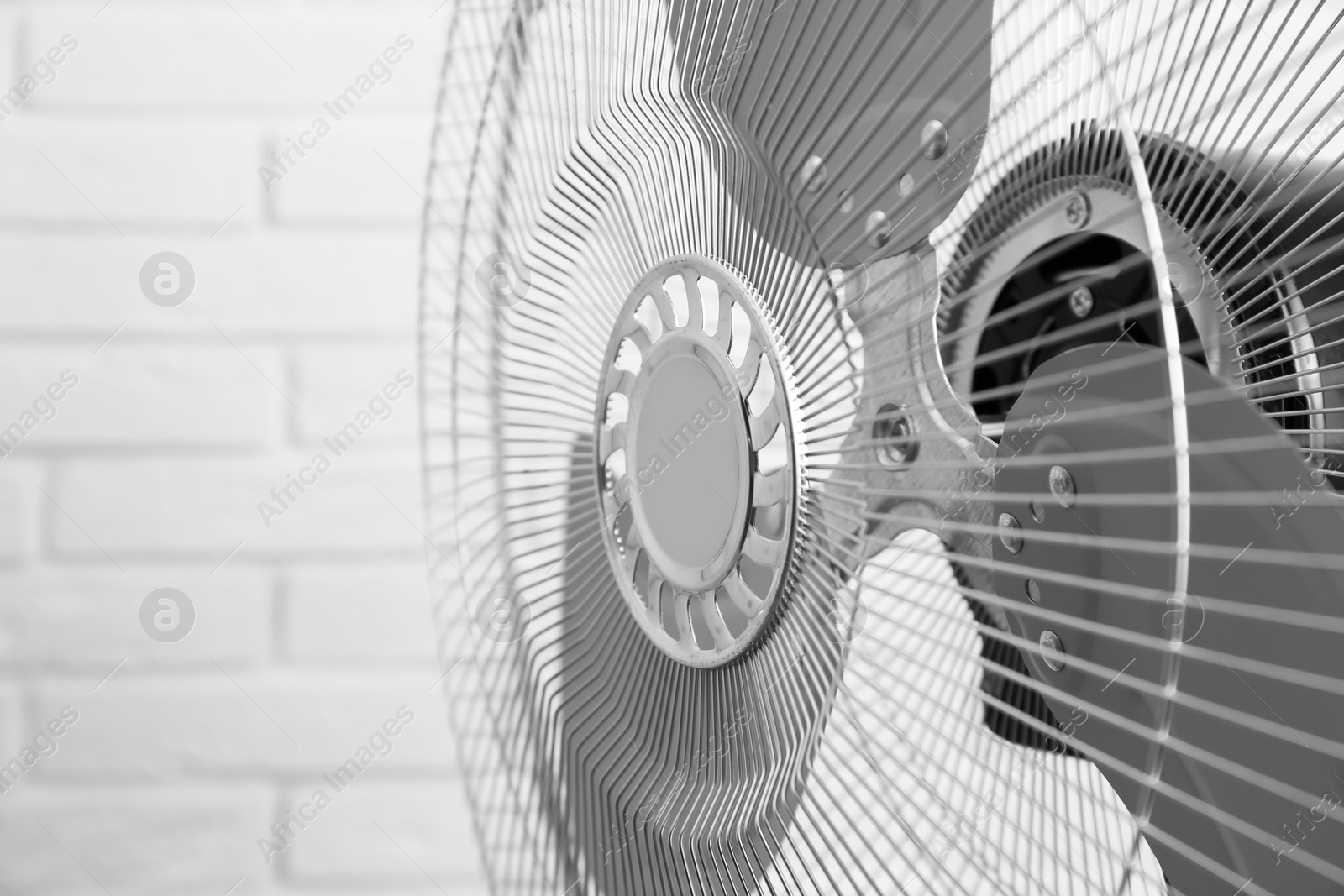 Photo of Electric fan near white brick wall, closeup. Summer heat