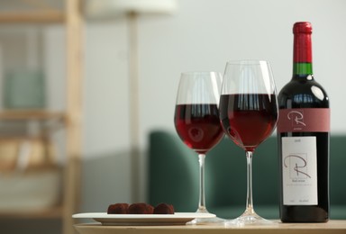 Photo of Bottle and glassesred wine with chocolate candies on wooden table in living room. Space for text