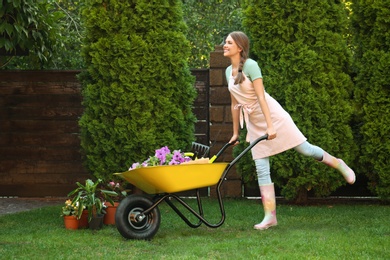 Photo of Happy young woman with wheelbarrow working in garden