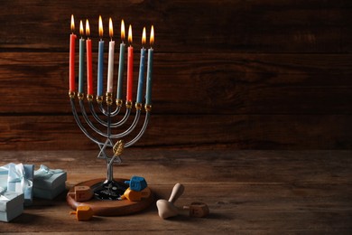 Photo of Hanukkah celebration. Menorah with burning candles, dreidels and gift boxes on wooden table, space for text