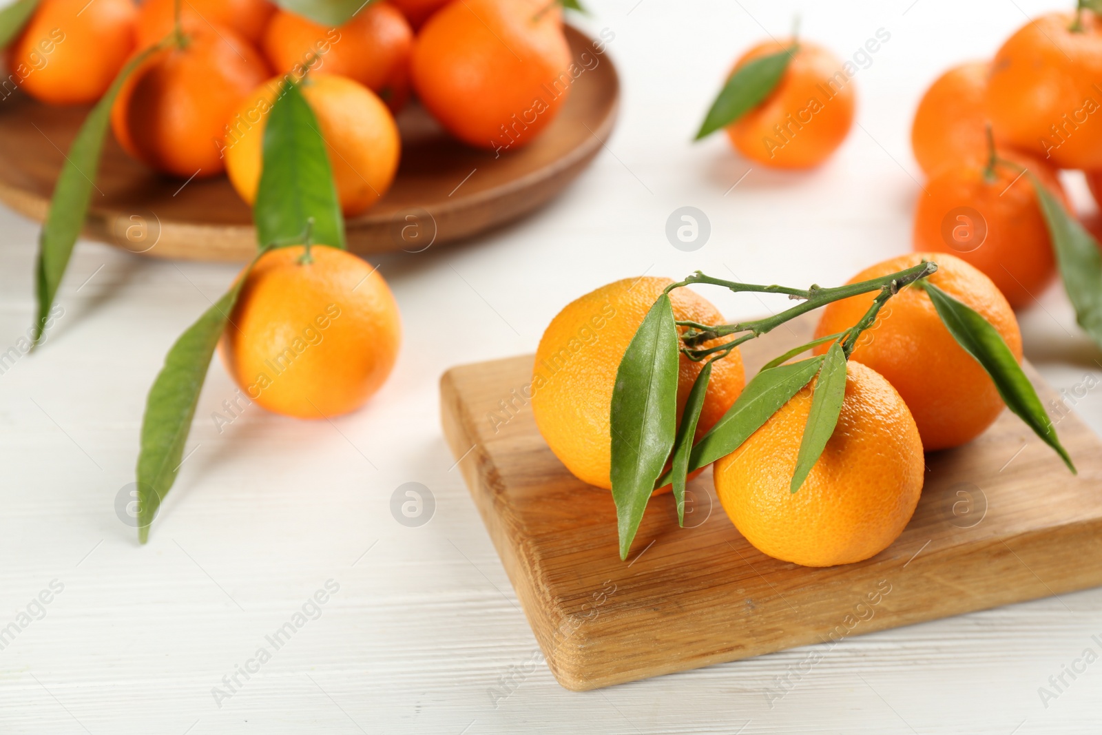 Photo of Fresh ripe tangerines with green leaves on white wooden table