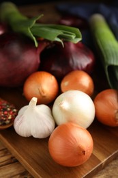 Photo of Fresh onion bulbs, leek, garlic and peppers mix on wooden table, closeup