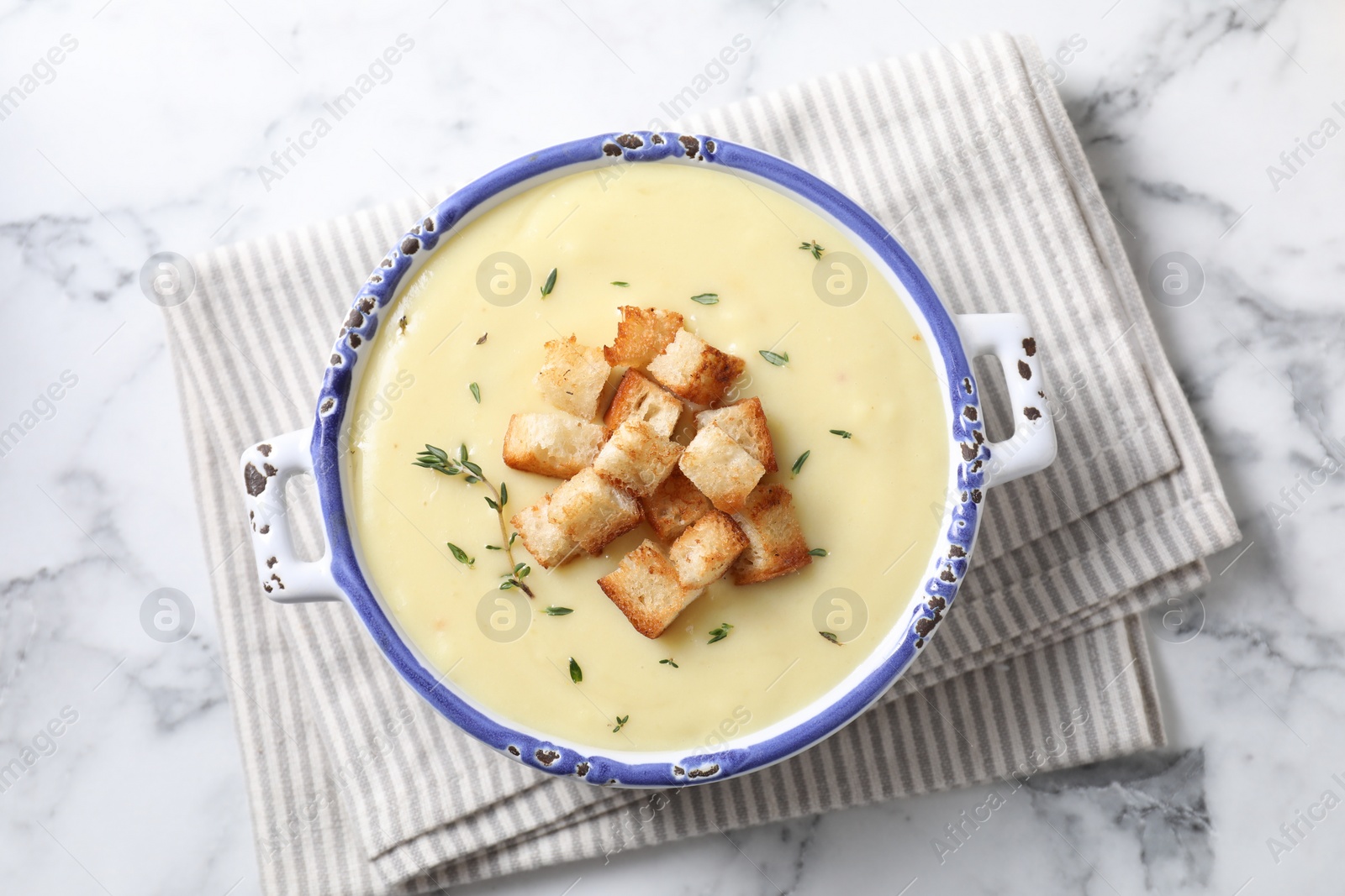 Photo of Tasty potato soup with croutons and rosemary in ceramic pot on white marble table, top view