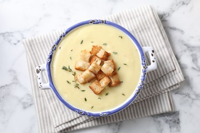 Photo of Tasty potato soup with croutons and rosemary in ceramic pot on white marble table, top view