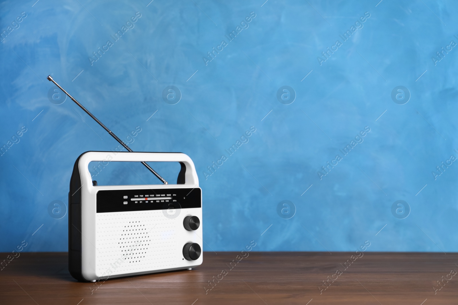 Photo of Retro radio receiver on wooden table against light blue background. Space for text