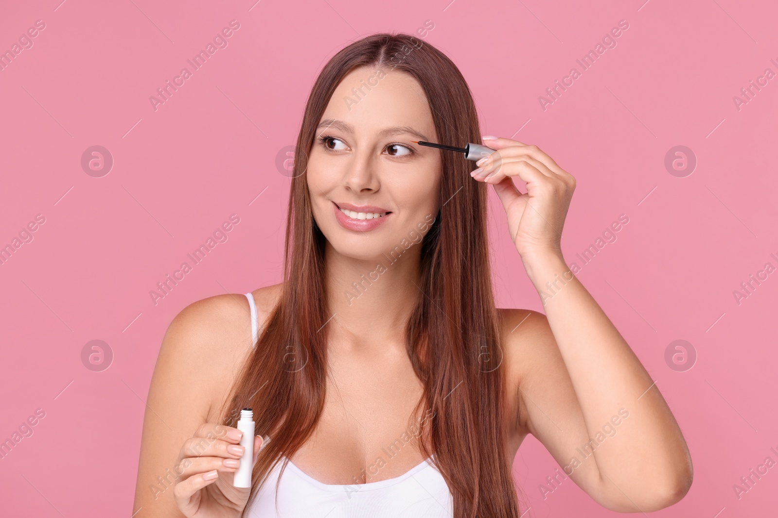 Photo of Beautiful woman applying serum onto eyelashes on pink background