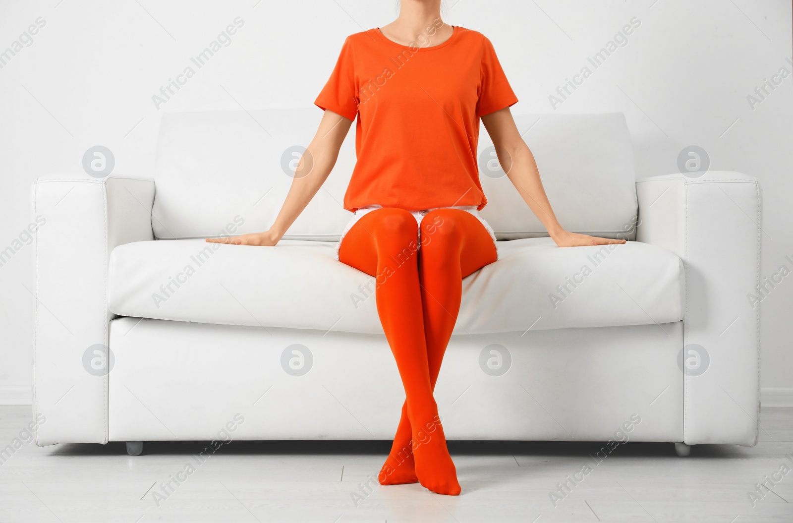 Photo of Woman wearing orange tights sitting on sofa indoors, closeup