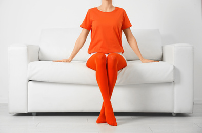 Photo of Woman wearing orange tights sitting on sofa indoors, closeup