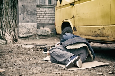Poor homeless man lying near van outdoors