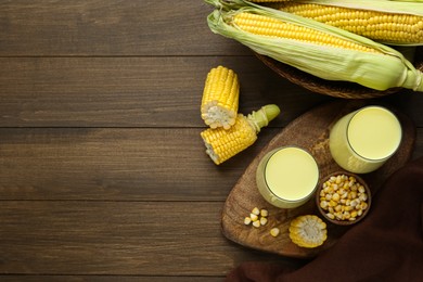 Photo of Tasty fresh corn milk in glasses and cobs on wooden table, flat lay. Space for text