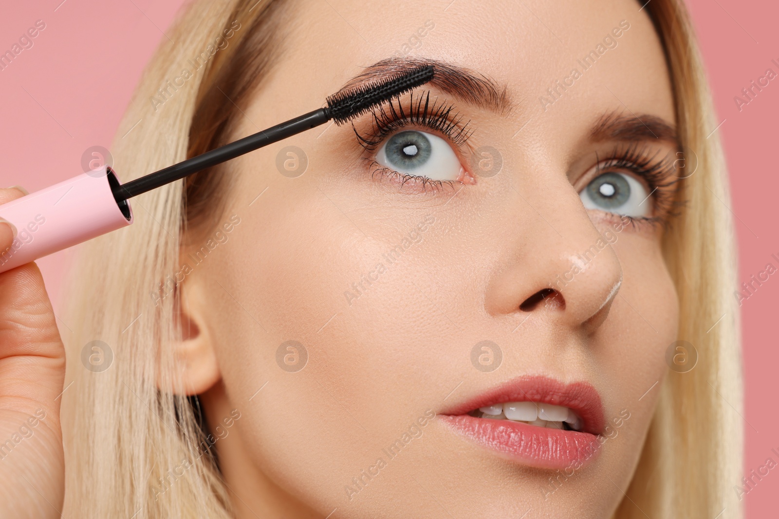 Photo of Beautiful woman applying mascara on pink background, closeup