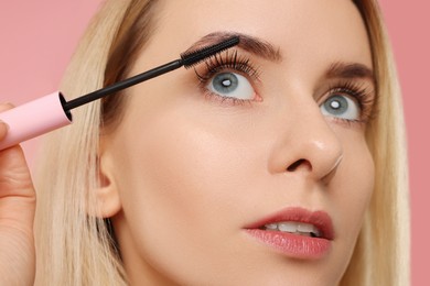 Beautiful woman applying mascara on pink background, closeup