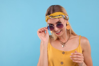 Photo of Portrait of smiling hippie woman in sunglasses on light blue background. Space for text
