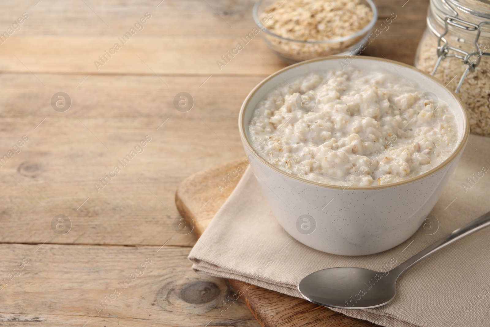 Photo of Tasty boiled oatmeal in bowl and spoon on wooden table, space for text