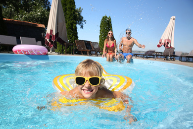 Photo of Little boy swimming with inflatable ring near his parents in outdoor pool on sunny summer day